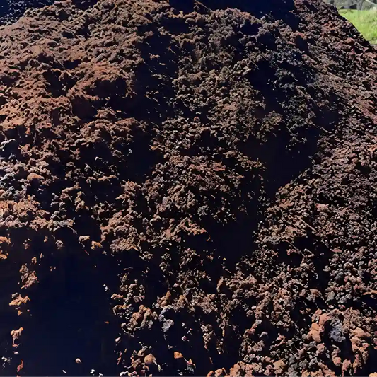 A close-up view of a large pile of dark brown and black compost or soil material under bright daylight.